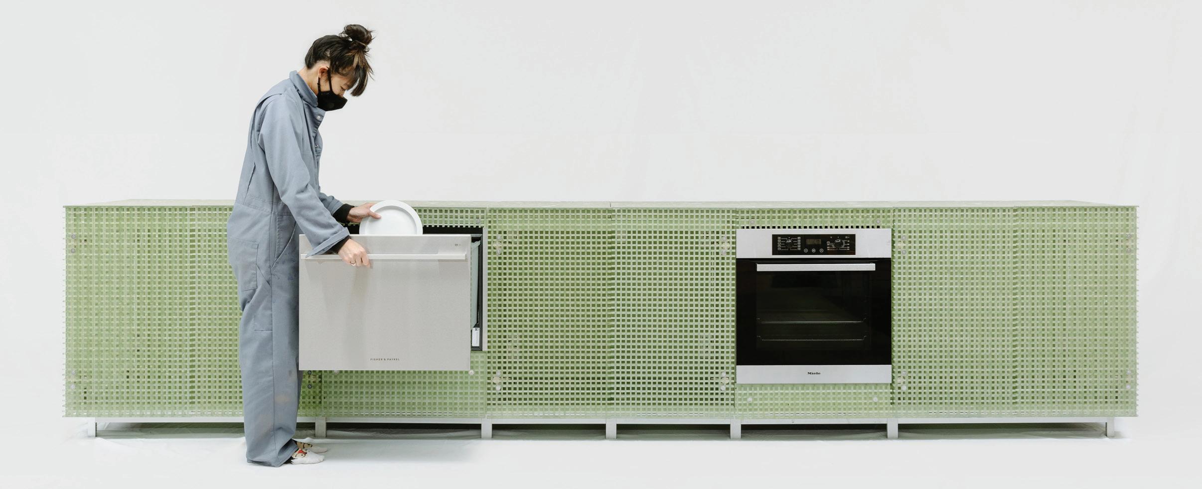 A woman stacks a dishwasher in a kitchen made of recycled materials.