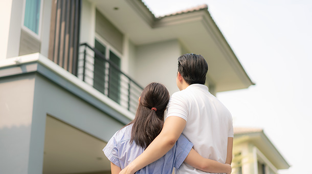 Back portrait of Asian young couple standing and hugging together looking happy in front of their new house to start new life.