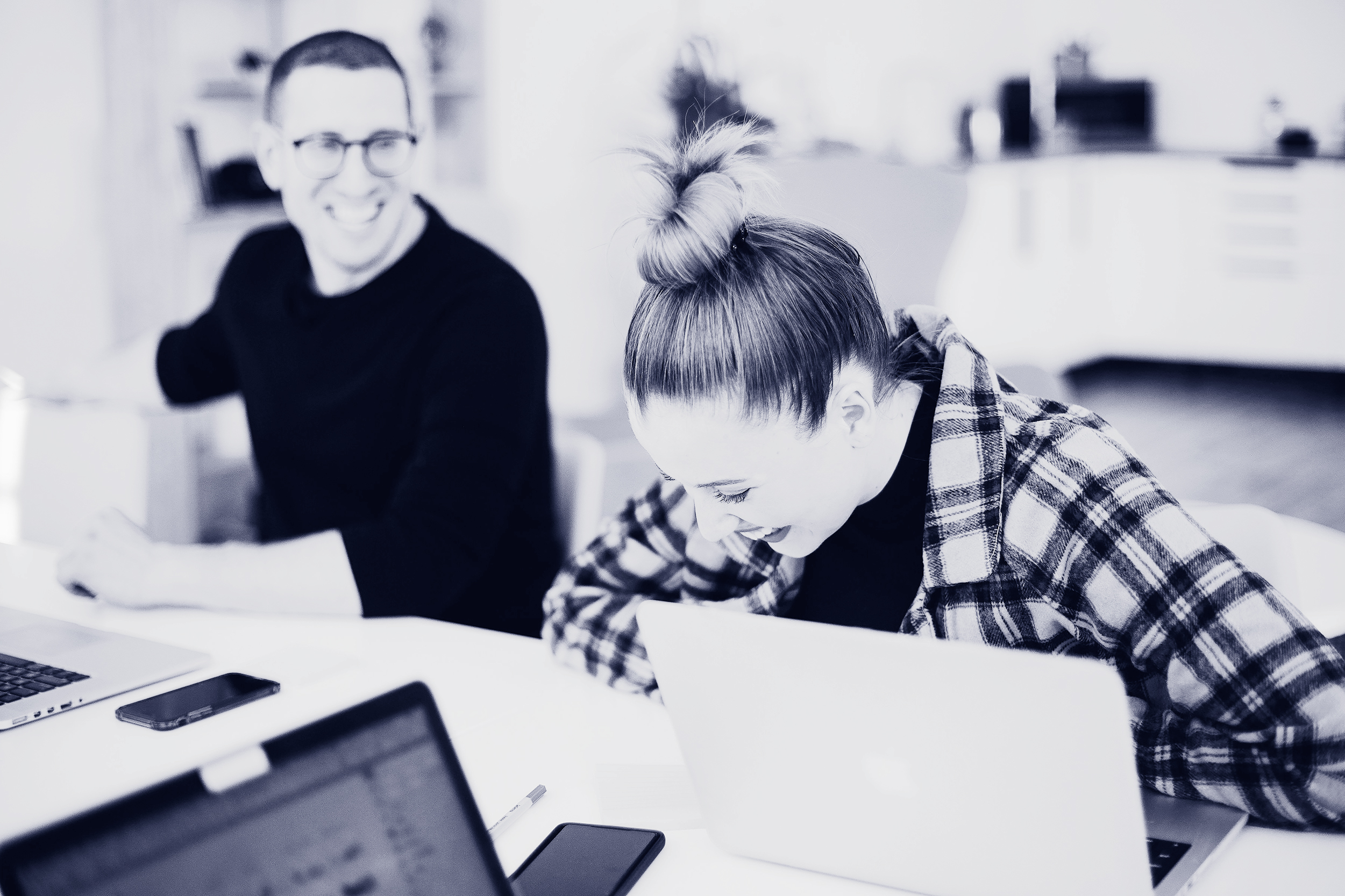 Two people sitting at a table with laptops laughing